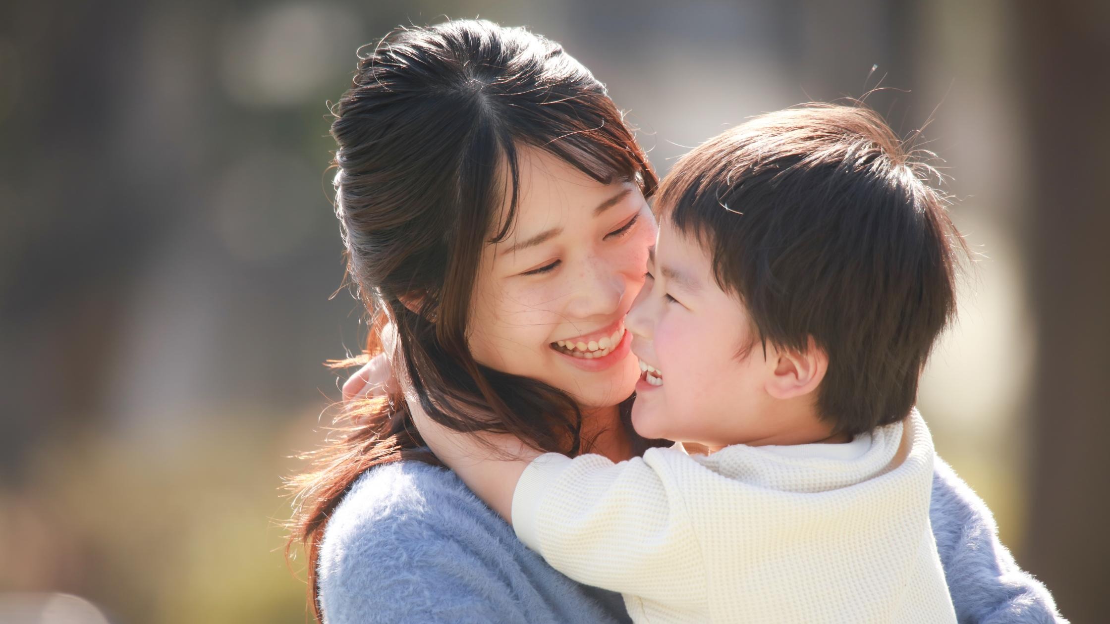 Smiling mother and child embracing outdoors, symbolizing care and family connection.