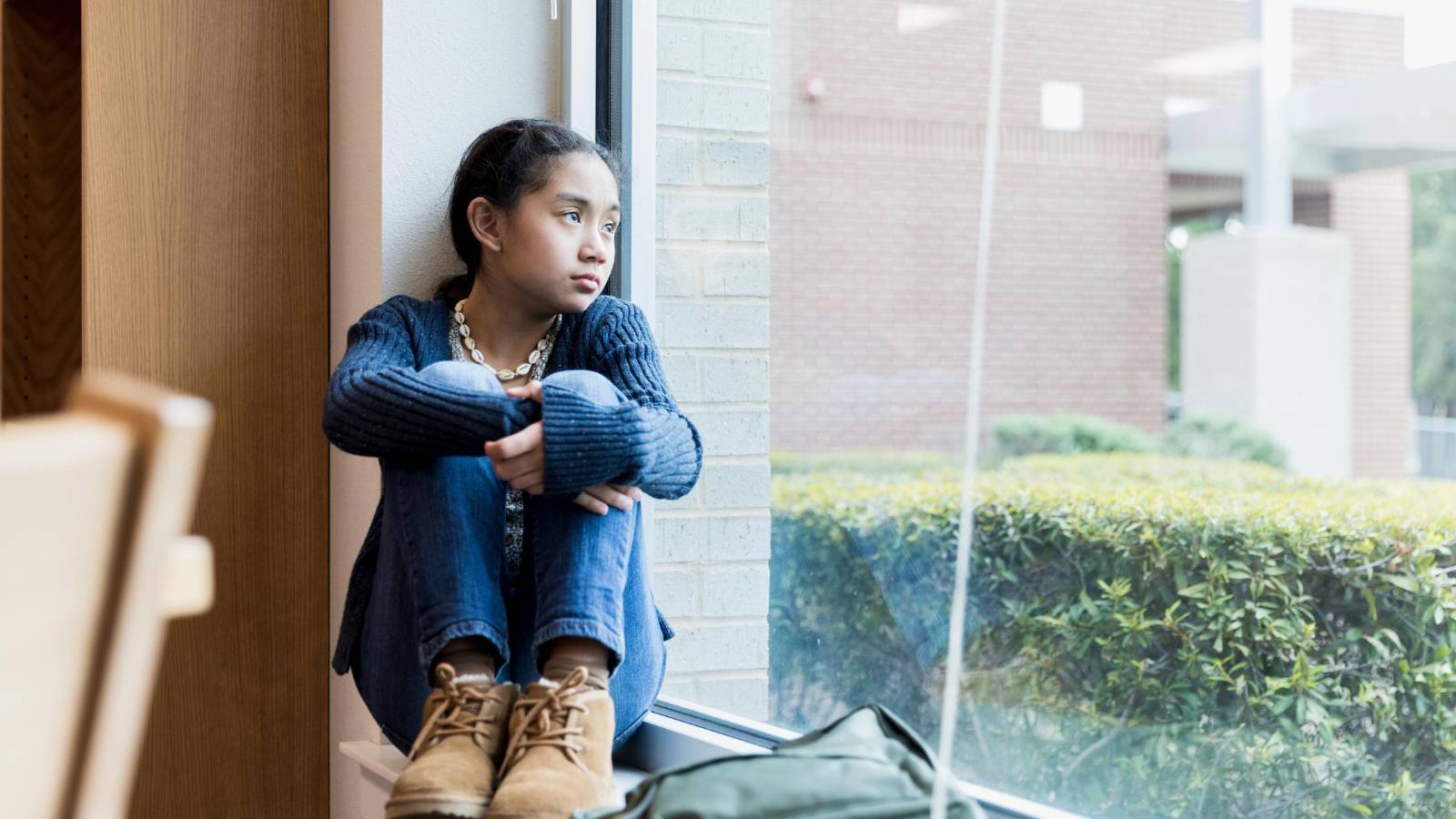 Young girl sitting by a window, looking thoughtful and isolated, reflecting the emotional challenges of families during the holiday season