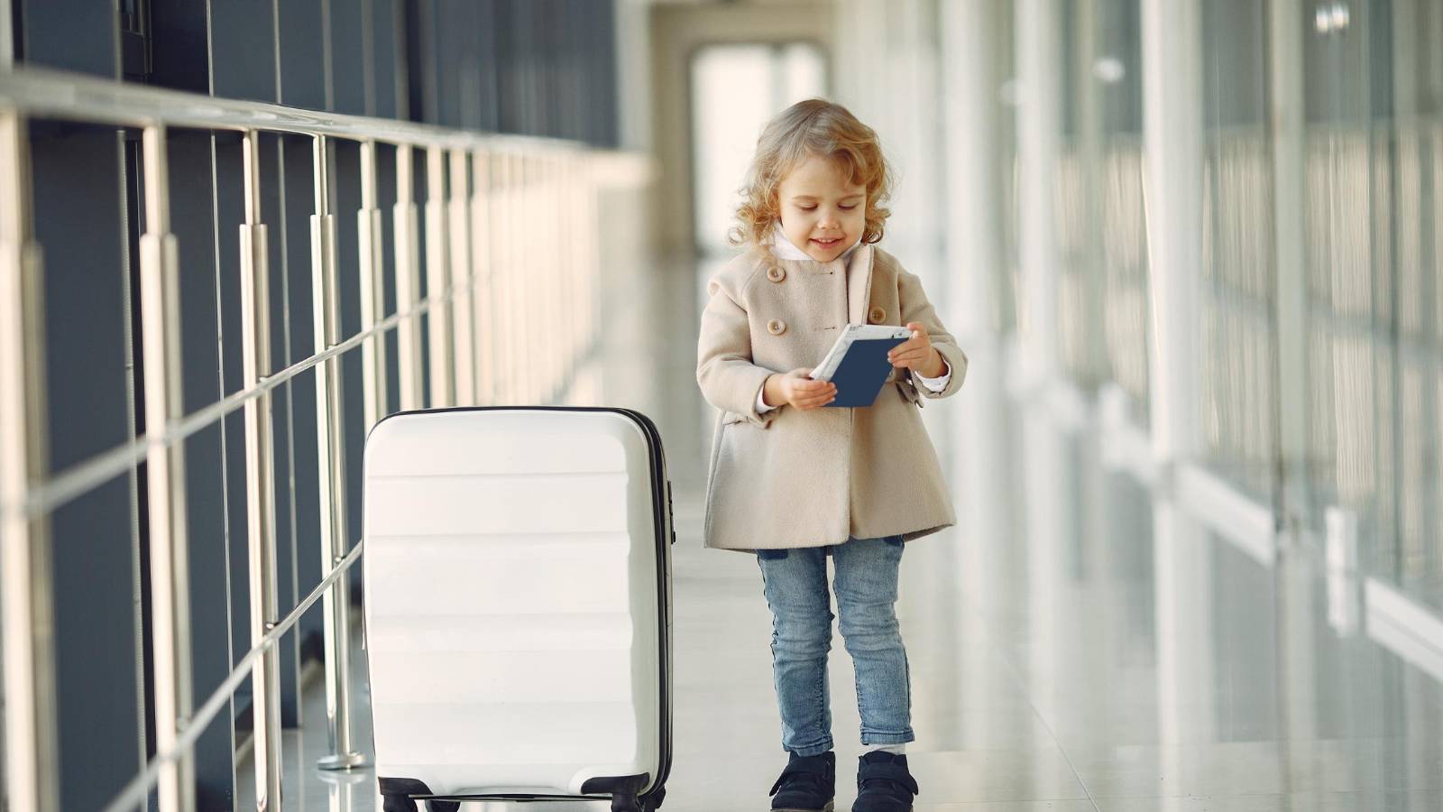 A young child with a suitcase and passport standing in an airport, symbolizing international travel.