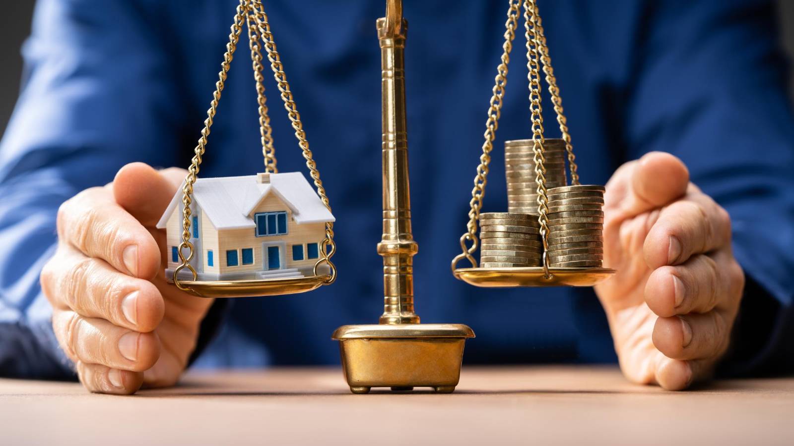 A balanced scale showing a house on one side and stacked coins on the other, symbolizing property and asset division in divorce.